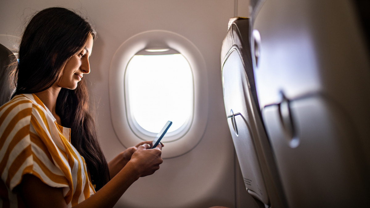 Young smiling Latin woman using mobile phone in the airplane.