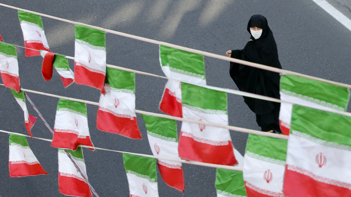 A koronavírus-járvány miatt védőmaszkot viselő nő halad el felfüggesztett iráni zászlók közelében az 1979-es iráni iszlám forradalom 42. évfordulója alkalmából tartott megemlékezésen Teheránban 2021. február 10-én, egy nappal az évforduló előtt.
