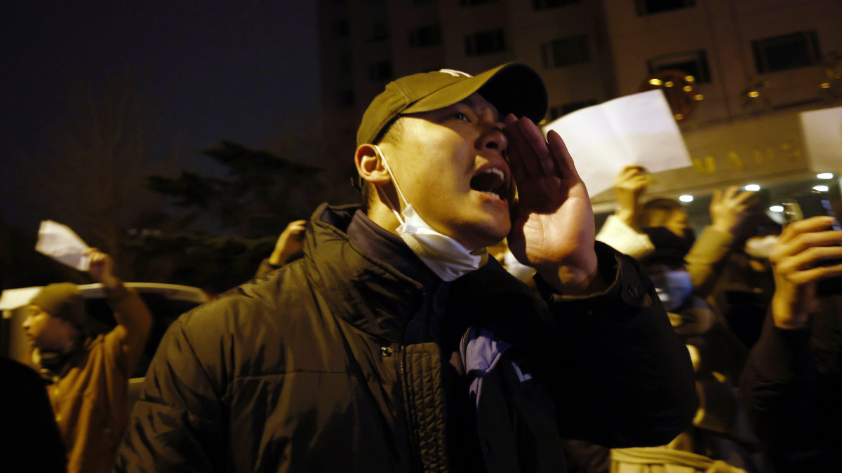 Tüntetők vonulnak Pekingben 2022. november 27-én. A tüntetők a kínai kormány koronavírus elleni óvintézkedései miatt tiltakoznak azt követően, hogy november 24-én a nyugat-kínai Hszincsiang-Ujgur Autonóm Terület székhelyén, Ürümcsiben kigyulladt egy 15 emeletes lakóépület. A tűzben - amelyet a vizsgálat szerint egy meghibásodott konnektor okozott - tízen életüket vesztették, és többen megsérültek. Az interneten keringő hírek szerint az áldozatok száma azért volt ilyen magas, mert az épületet részleges vesztegzár alá helyezték, és a lakók nem tudtak időben kimenekülni. Városi tisztségviselők ezt tagadták. A négymillió lakosú Ürümcsiben vannak, akik már száz napja karanténban vannak.