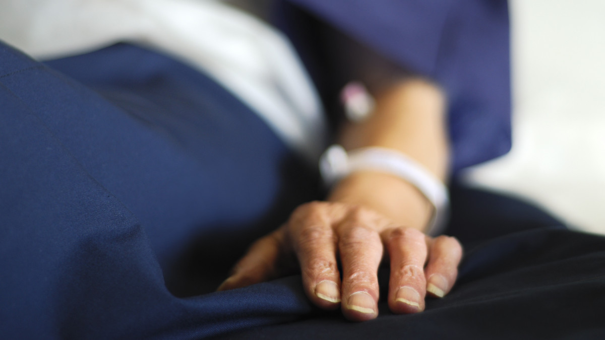 Closeup of an older persons hand on a hospital bed. Person is awaiting surgery.  ID Bracelet and intravenous connections shown, Very Shallow DoF - focus is on fingernails and fold in fabric.