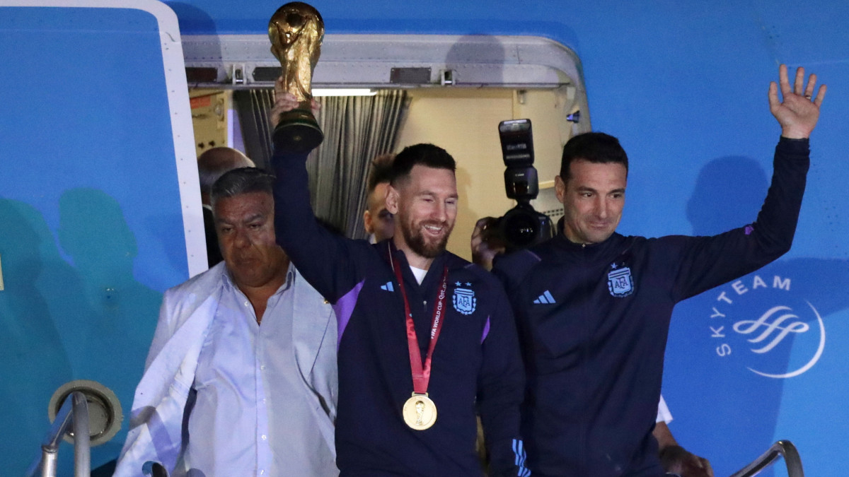 Lionel Messi argentin csapatkapitány (k) kezében a bajnoki trófeával és Lionel Scaloni szövetségi kapitány (j), miután a válogatott játékosaival megérkeztek a Buenos Aires-i Ezeiza repülőtérre 2022. december 20-án. Argentína két nappal korábban 4-2-re győzött a katari labdarúgó-világbajnokság döntőjében játszott Argentína-Franciaország mérkőzés 3-3-as hosszabbítása utáni tizenegyes-párbajban.