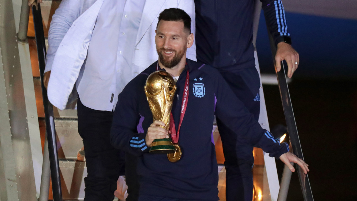 Lionel Messi argentin csapatkapitány kezében a bajnoki trófeával, miután a válogatott játékosaival megérkezett a Buenos Aires-i Ezeiza repülőtérre 2022. december 20-án. Argentína két nappal korábban 4-2-re győzött a katari labdarúgó-világbajnokság döntőjében játszott Argentína-Franciaország mérkőzés 3-3-as hosszabbítása utáni tizenegyes-párbajban.