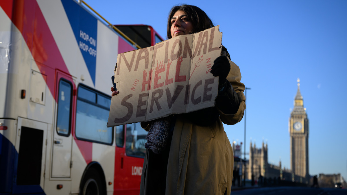 LONDON, ENGLAND - DECEMBER 15: A woman holds a placard as nurses and supporters gather to demonstrate outside St Thomas hospital in Westminster on December 15, 2022 in London, England. Nurses in England, Wales and Northern Ireland have begun the first of two day-long strikes over pay and working conditions, with a second taking place on 20 December. (Photo by Leon Neal/Getty Images)