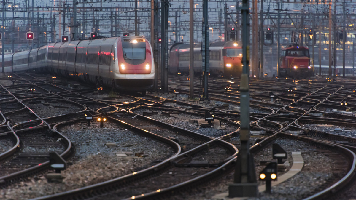In the early morning twilight, several commuter trains are approaching a busy railway station.