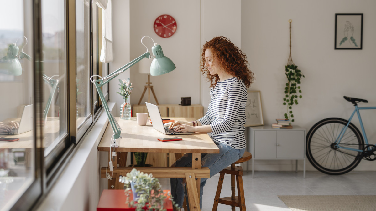 Woman sitting on a desk using a laptop computer while working from home. Business, freelance and home office concept.