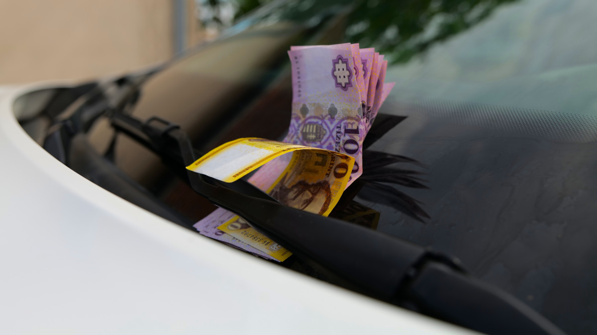 Hungarian forint banknotes on the front windshield of a white car right under the windshield wiper. On the picture there are five and ten thousand forint banknotes, altogether 115000 HUF.