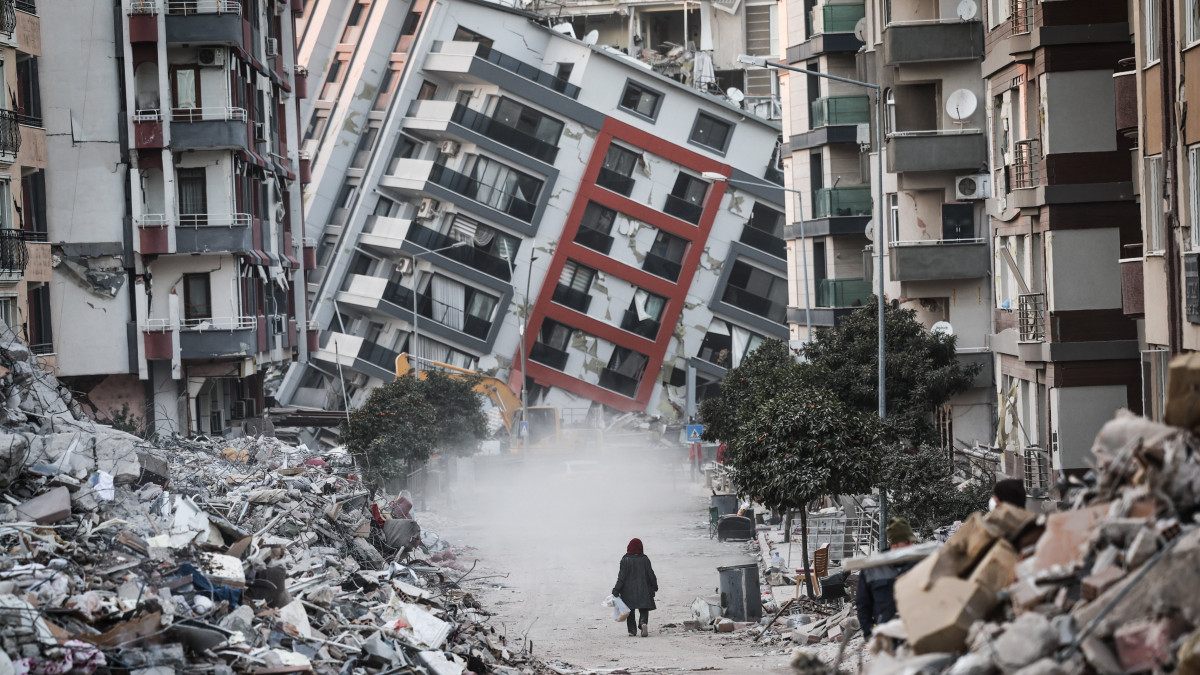 Összedőlt ház előtt egy nő a törökországi Hatayban 2023. február 17-én, tizenegy nappal a Dél-Törökországot és Észak-Szíriát sújtó 7,7-es és 7,6-es erősségű két földrengés után. A természeti katasztrófa halálos áldozatainak száma meghaladja a 42 ezret.