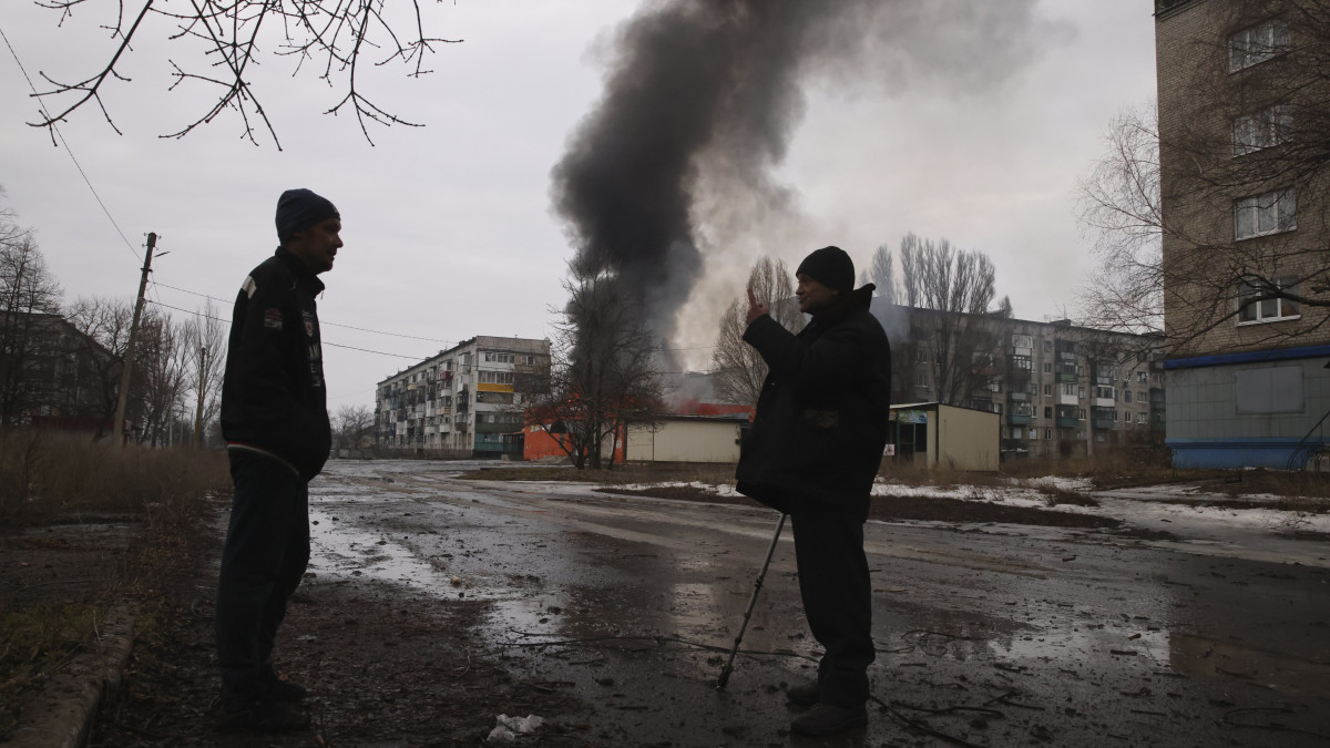 Égő ház előtt beszélget két férfi a kelet-ukrajnai Donyecki területen fekvő, az orosz hadsereg által ostromlott Bahmutban 2023. február 27-én.