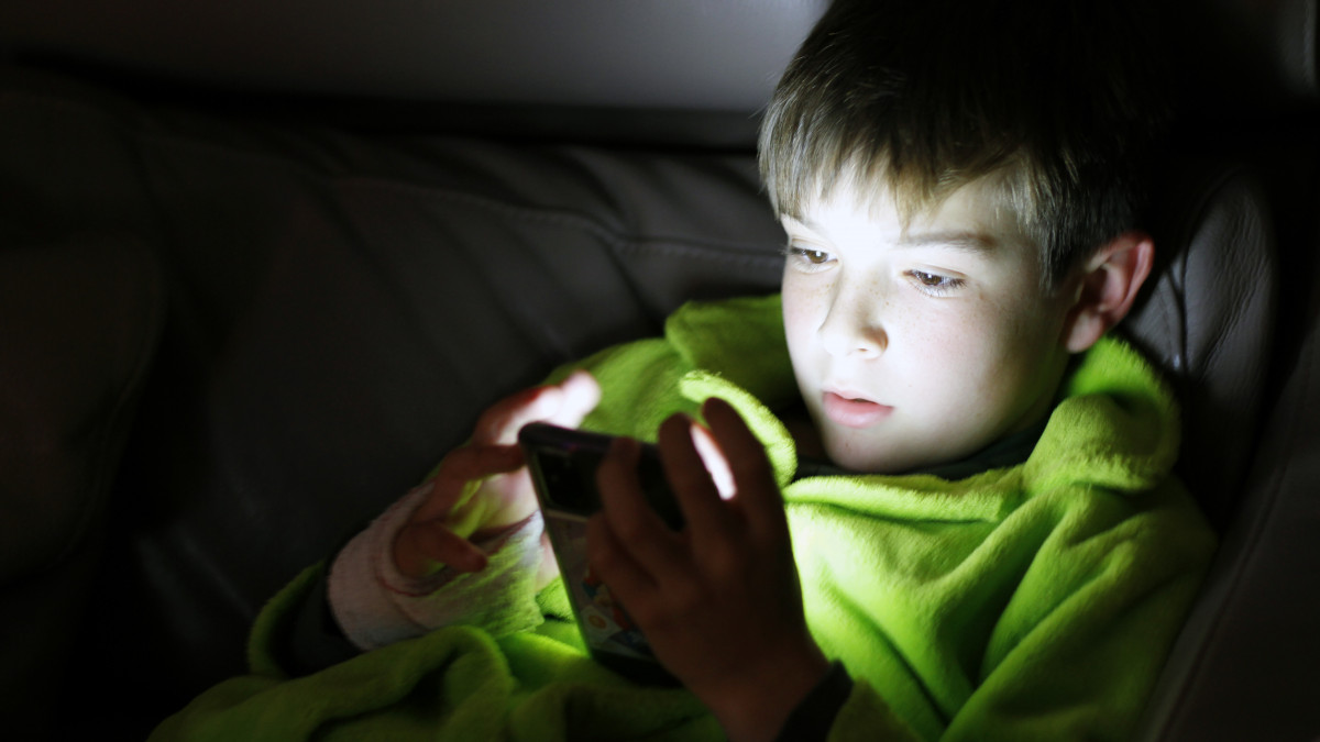 Boy using smartphone on sofa at night