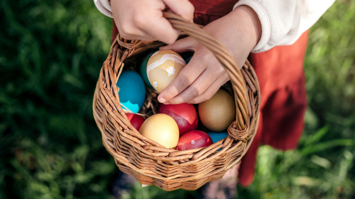 Little girl hands holding multicolored Easter eggs in the basket outdoors. Close-up.