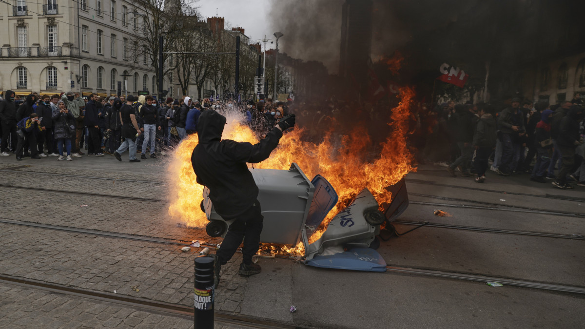 A nyugdíjreform ellen tüntetők egyike egy felgyújtott szemetesedény mellett a nyugat-franciaországi Nantes-ban a francia szakszervezetek által meghirdetett egynapos országos sztrájk alatt, 2023. március 23-án. Emmanuel Macron elnök széles körű felháborodást váltott ki azzal, hogy parlamenti szavazás nélkül készül hatályba léptetni a nyugdíjkorhatár 62-ről 64 évre emelését előirányzó törvényt.