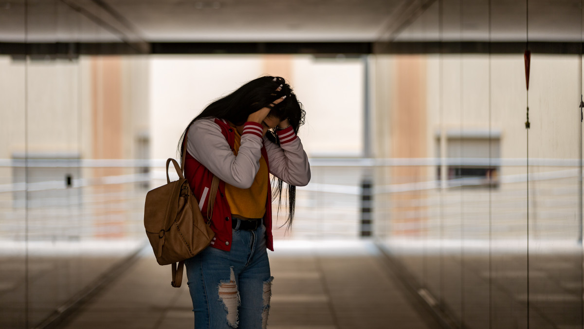 Side view of teen girl in casual clothing with backpack standing in corridor while worried about bullying at school feeling lonely