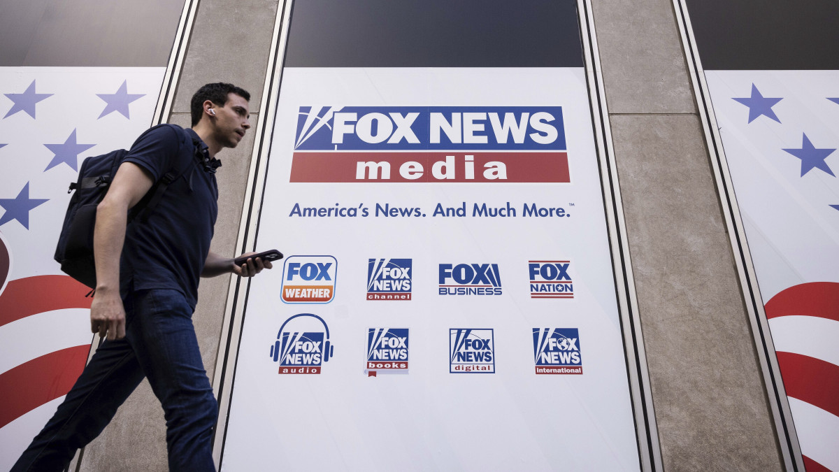 A Fox News amerikai hírtelevízió New York-i székháza előtt egy járókelő 2023. április 12-én. A televízió ellen indított rágalmazási per tárgyalása 2023. április 18-án kezdődik a Delaware állambeli Wilmingtonban. A Fox Newst 1,6 milliárd dollárra perli az elektronikus szavazási hardvereket és szoftvereket gyártó Dominion Voting Systems, amiért szerinte a televízió bizonyos munkatársai szándékosan felerősítették Donald Trump volt amerikai elnök egyes támogatóinak állításait, amelyek szerint a Dominion által gyártott szavazógépek meghamisították a 2020-as elnökválasztáson leadott voksokat.