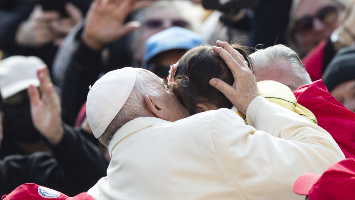 Ferenc pápa megpuszil egy gyermeket hetenkénti általános kihallgatásán a vatikáni Szent Péter téren 2023. április 19-én.