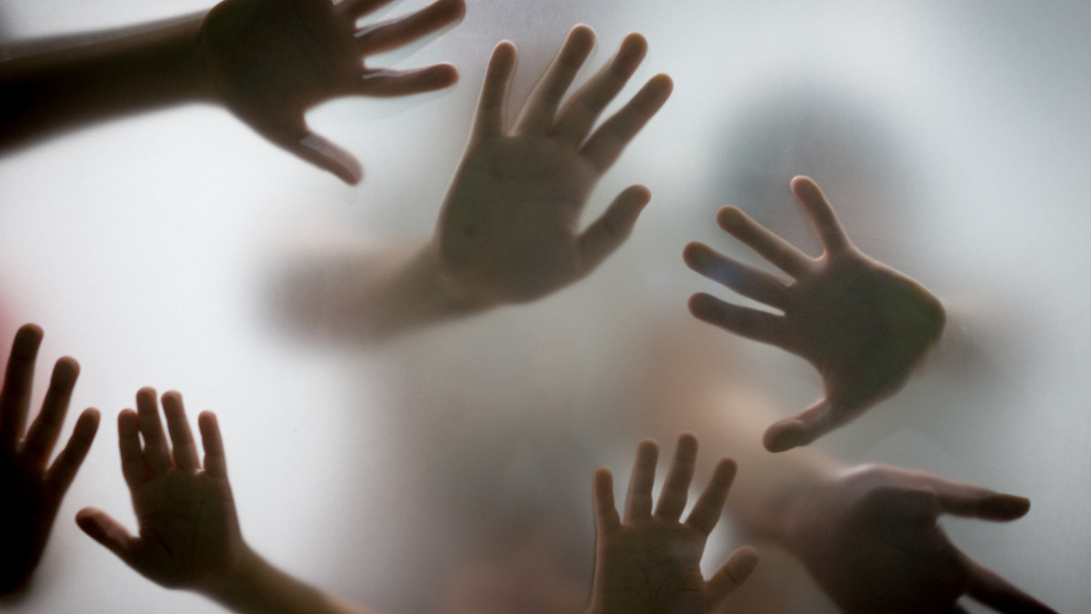 Many hands in silhouette pressed against frosted glass