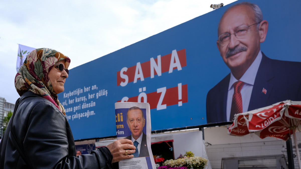 Kemal Kilicdaroglut, a török ellenzéki Köztársasági Néppárt (CHP) elnökét, egy hatpárti ellenzéki pártszövetség elnökjelöltjét ábrázoló plakát előtt osztogatja Recep Tayyip Erdogan török elnök reklámanyagát egy aktivista Isztambulban 2023. május 10-én, négy nappal a török elnökválasztás első fordulója előtt. Május 14-én parlamenti választásokat is tartanak Törökországban.