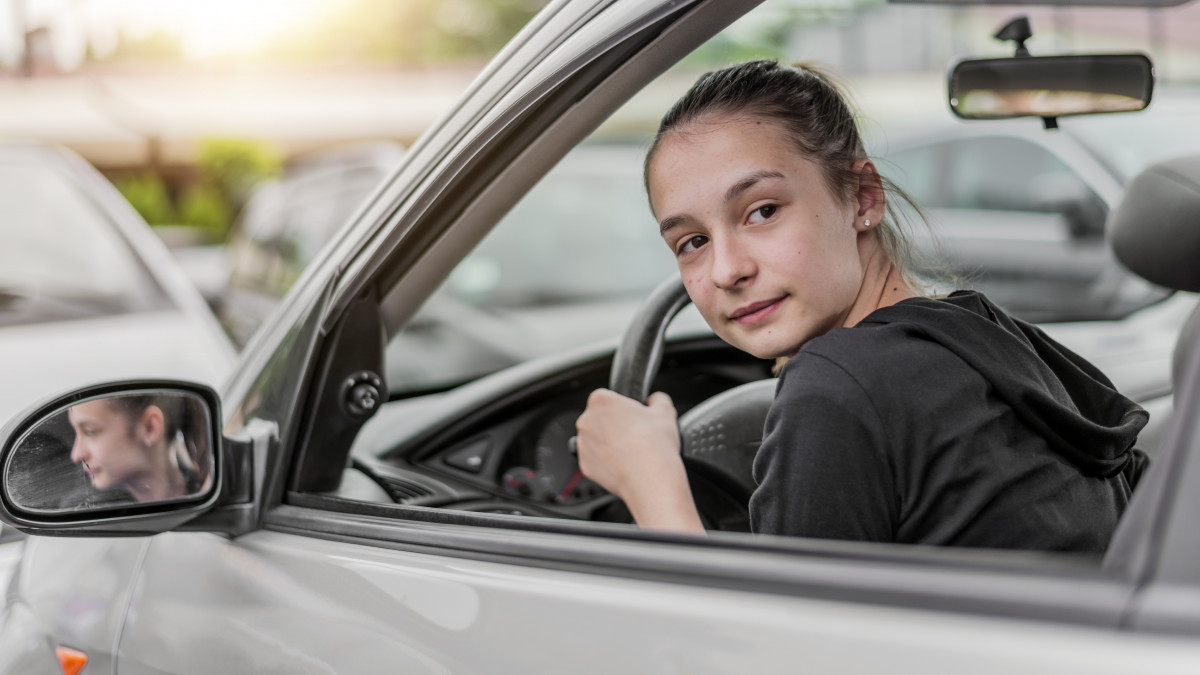 Beautiful, confident teen girl behind the wheel of her car.Teenage girl behind steering looking over shoulder to back seat at sunset and parking car.