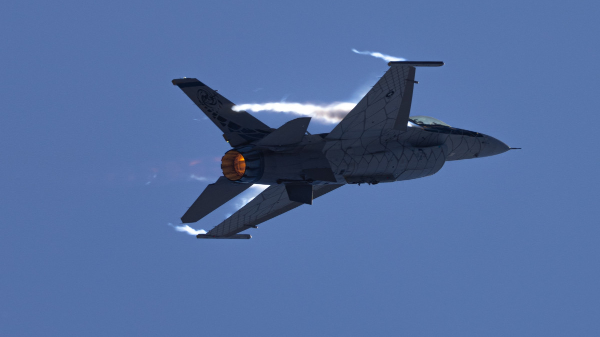Close tail view of a F-16 Fighting Falcon in a high G maneuver, with condensation streaks at the wing roots and afterburner on