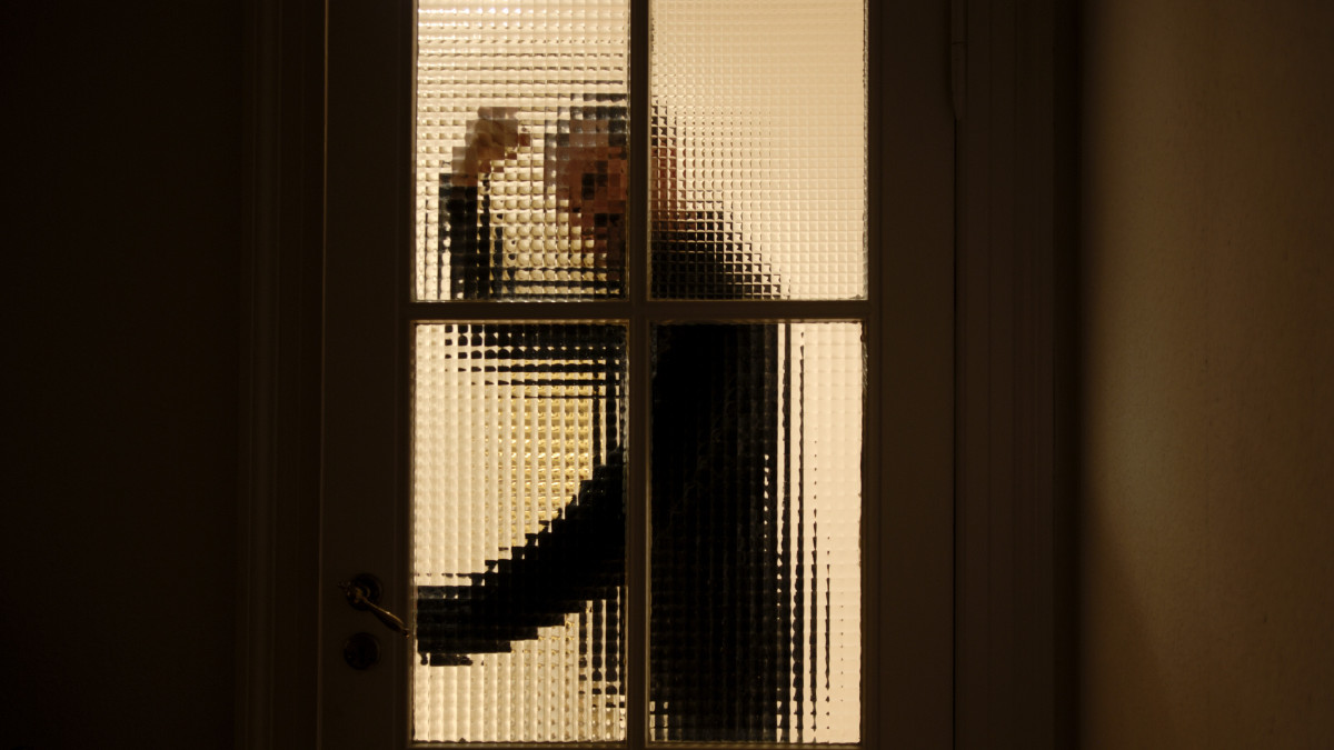 An aggressive and violent man on his way through a partially transparent glass door (entering a dark room).