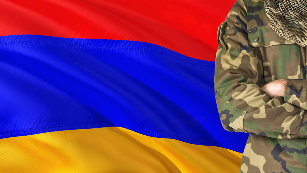 Crossed arms Armenian soldier with national waving flag on background - Armenia Military theme.