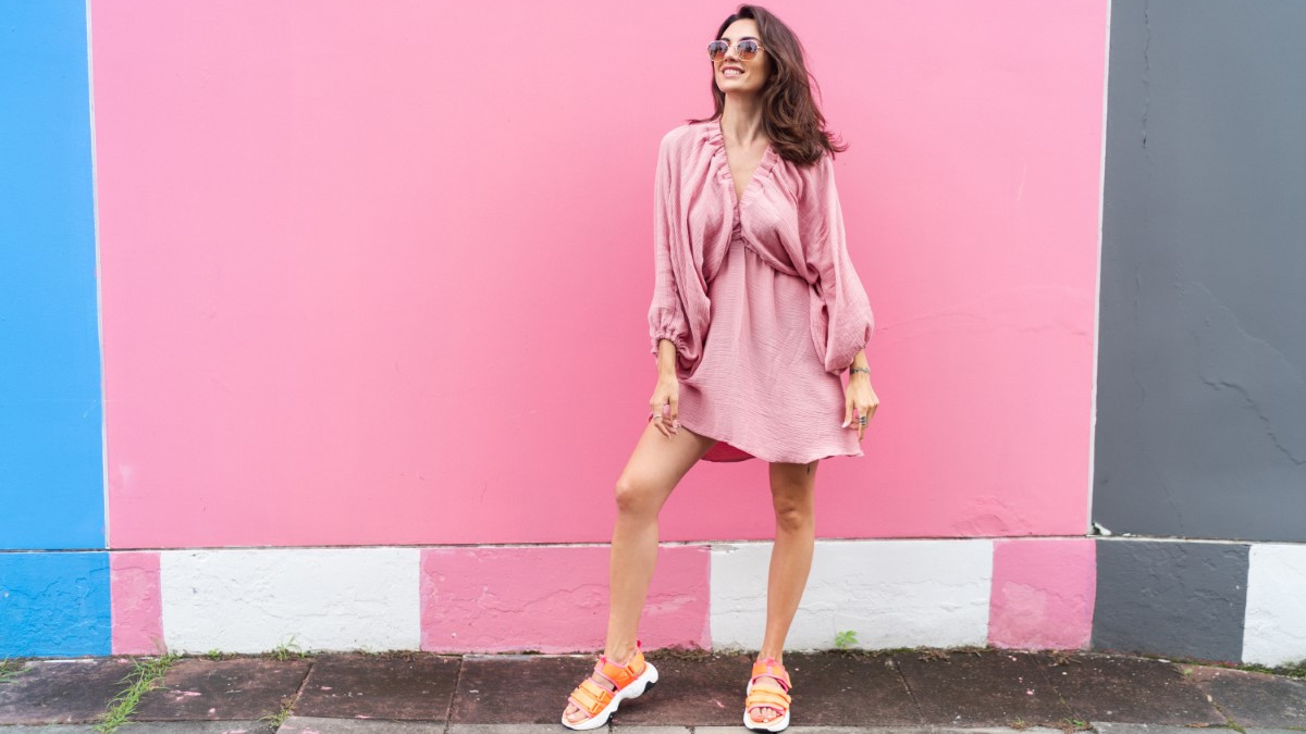 Young beautiful smiling cute romantic woman in trendy summer dress. Carefree woman posing in the street near pink wall. Positive model outdoors in sunglasses. Cheerful and happy