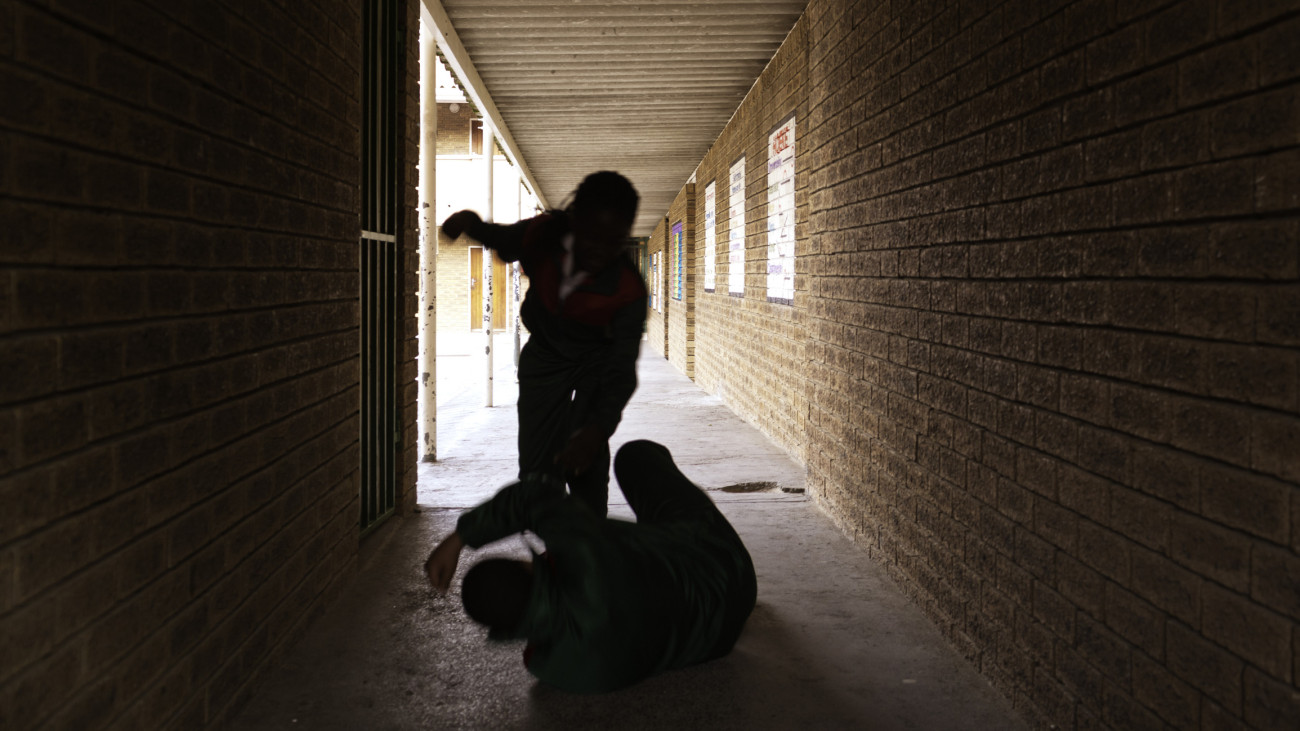 Two school kids fight in a dark passageway of their school, almost silhouette.