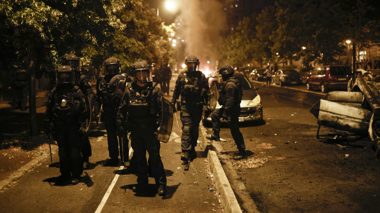 Rohamrendőrök könnygáz és lángoló autók füstjében oszlatnak egy tüntetést Párizs Nanterre nevű elővárosában 2023. június 29-re virradóan. Az erőszakossá fajult újabb tüntetésen amiatt romboltak és gyújtogattak, hogy június 27-én egy rendőr intézkedés közben lelőtt egy 17 éves fiatalt a városban. A hatóságok több tucat tüntetőt elvezettek. A fiatal életét kioltó rendőr ellen vizsgálat kezdődött.