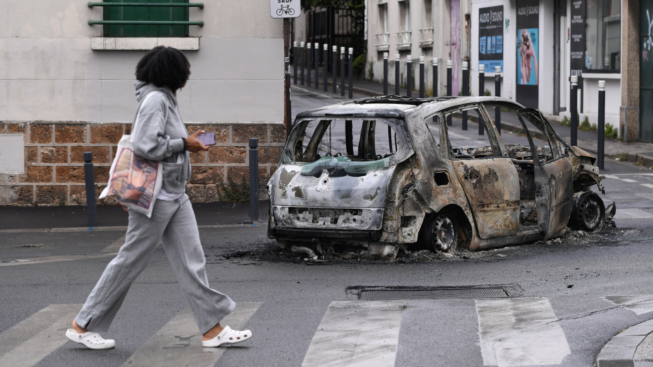 Tüntetők által felgyújtott autó roncsát nézi egy járókelő a Párizs közelében levő Montreuil-ben 2023. július 1-jén, a nanterre-i incidens után négy nappal. Június 27-én egy közúti ellenőrzést végző rendőr intézkedés közben lelőtt egy 17 éves fiatalt Párizs Nanterre nevű elővárosában. Az eset miatt több francia városban az egymást követő negyedik éjszaka gyújtogattak és fosztogattak a tüntetők. A kormány válságtanácskozást tartott és 45 ezer rendőrt vezényelt Párizs és több francia nagyváros utcáira, hogy megfékezzék a pusztítást. Eddig több mint 1300 rendbontót vettek őrizetbe.