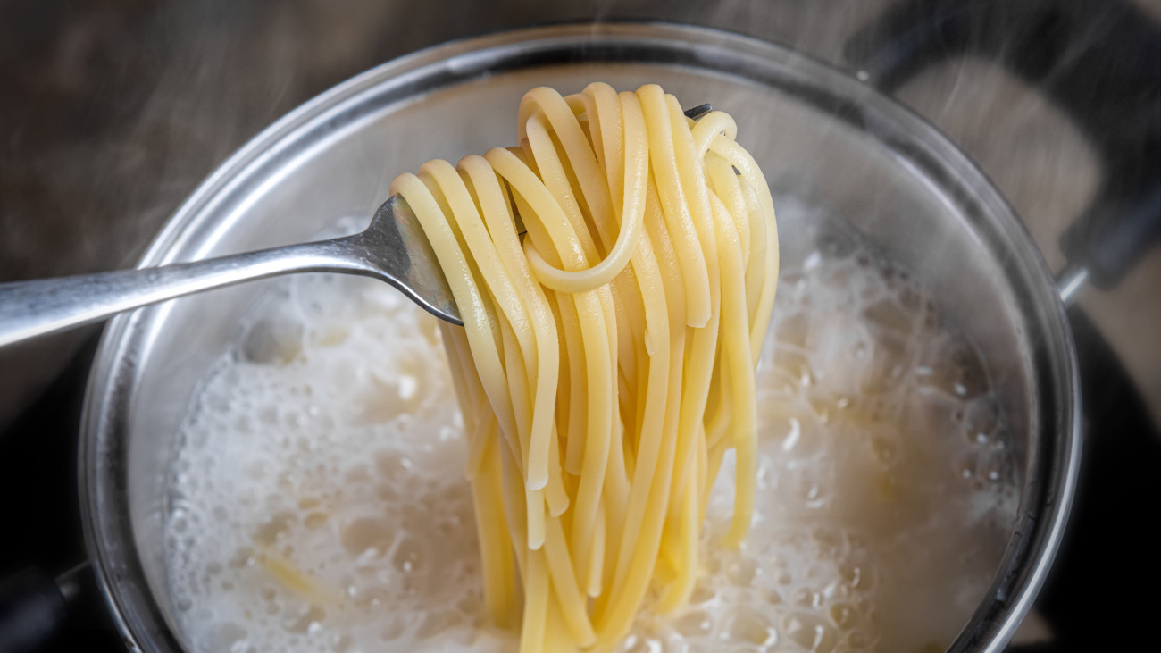Yellow noodles or spaghetti cooking in boiling water pot with indoor low lighting.