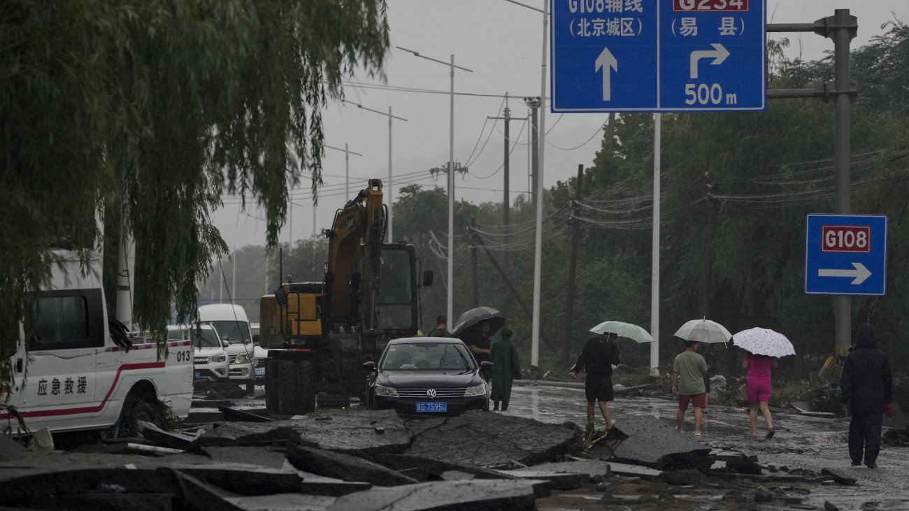 Emberek mennek a Doksuri tájfun okozta heves esőzések által elmosott utak egyikének maradványain a nyugat-pekingi Mentugu kerületben 2023. július 31-én. Több mint 31 ezer embert evakuáltak otthonaikból a kínai fővárosban, miután a Doksuri tájfun heves esőzést zúdított Pekingre és környékére, 180 pekingi repülőjáratot töröltek és több mint 350 fővárosi közút vált járhatatlanná, a Mentugu kerületben pedig a katasztrófavédelem két holttestet talált.