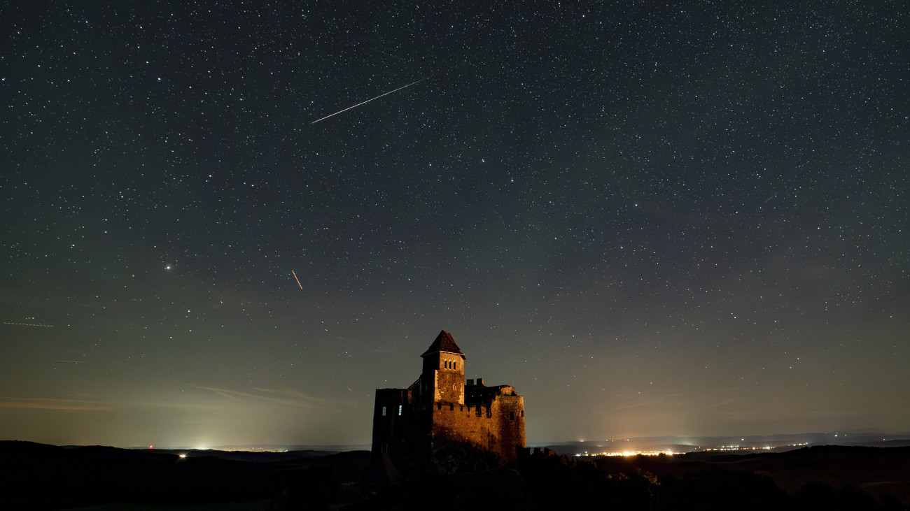 A hosszú expozíciós idővel készült képen csíkot húz az égen egy hullócsillag (felül) - alatta repülőgépek fényei - a hollókői vár felett 2023. augusztus 12-én, a Perseida meteorraj hullásának idején. A Perseidák az egyik legismertebb, sűrű csillaghullást előidéző meteorraj. A raj sok apró porszemcséből áll, amelyek a földi légkörben nagy sebességük következtében felhevülnek és elégnek.