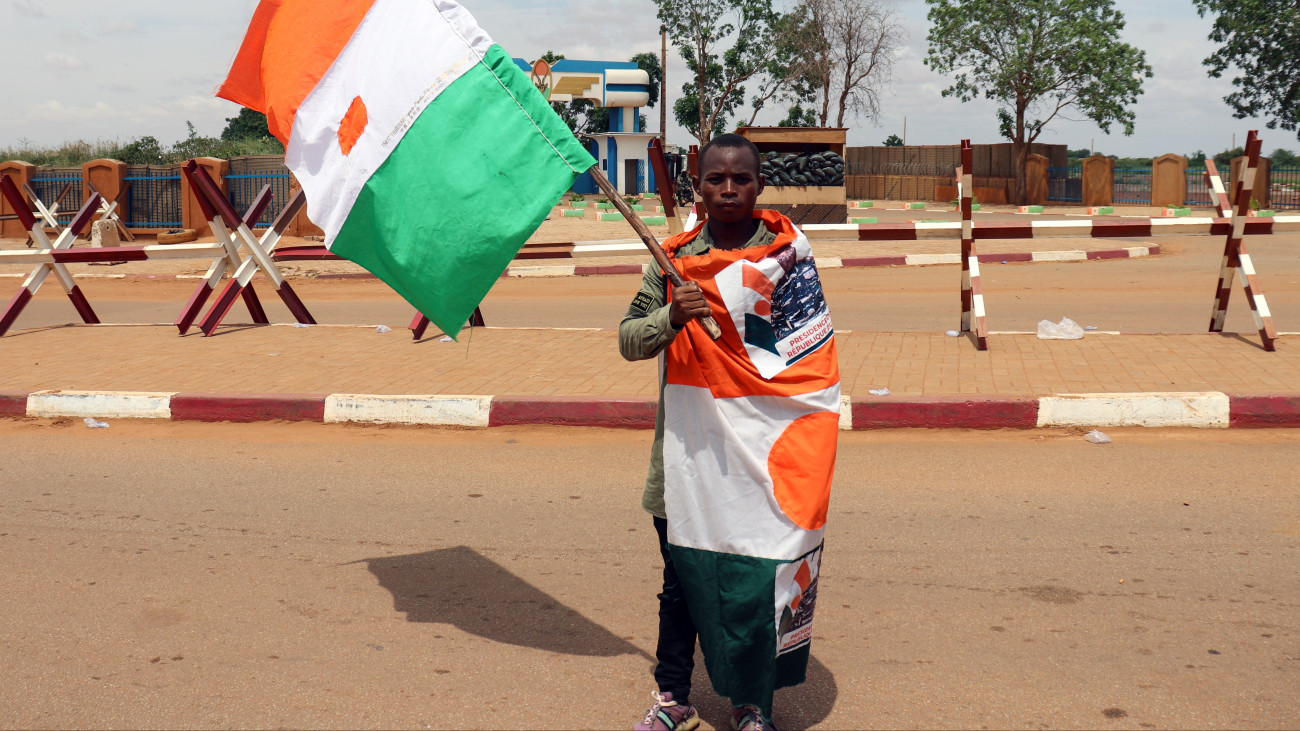 A nigeri junta egyik támogatója az ország zászlóját tartva tüntet a főváros, Niamey francia légitámaszpontjánál 2023. augusztus 27-én. A puccsiták augusztus 26-án kétnapos határidővel kiutasították az országból Franciaország nigeri nagykövetét, Sylvain Ittét. A hatalmat július 26-án magához ragadó junta azzal vádolta meg Franciaországot, hogy fegyveres beavatkozásra készül a fogságban levő Mohamed Bazoum nigeri elnök visszahelyezése érdekében, és azt állította, hogy a Nyugat-afrikai Államok Gazdasági Közössége (ECOWAS) az egykori gyarmattartó Franciaország zsoldjában áll. Az ECOWAS súlyos szankciókat rendelt el Niger ellen az államcsíny után, és azzal fenyegette meg a juntát, hogy hadsereget vet be az alkotmányos rend helyreállításáért. Franciaország 1500 katonát állomásoztat Nigerben.