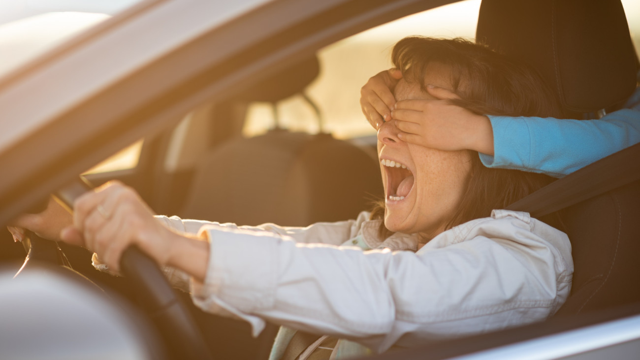 Kid covering eyes of her mother from behind while she is driving car