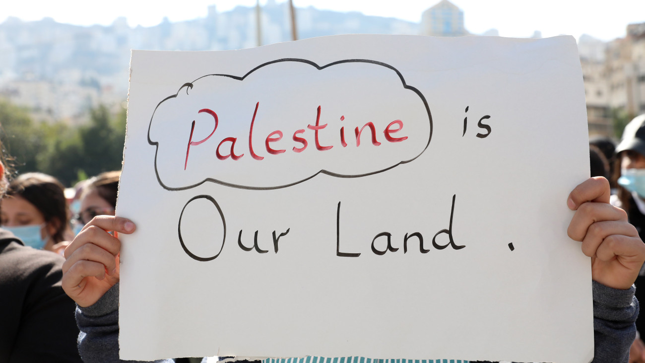 Palesztin férfi a magasba emel egy Palesztina a mi földünk feliratú plakátot egy bíróság épülete előtt az 1917-es Balfour-nyilatkozat miatt Nagy-Britannia ellen indított palesztin per első tárgyalási napján a ciszjordániai Nábluszban 2020. november 16-án. Palesztin ügyvédek keresetet nyújtottak be a szigetország ellen Lord Arthur Balfour egykori brit külügyminiszter deklarációja miatt, amelyben kifejezésre juttatta, hogy a brit kormány támogatja a zsidó törekvéseket egy zsidó nemzeti otthon létrehozására Palesztinában.