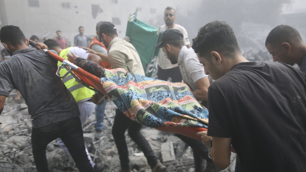 Sebesültet visznek a romok között palesztin férfiak egy izraeli légitámadás után a Gázai övezet déli részén fekvő rafahi menekülttáborban 2023. október 12-én. A Gázai övezetet irányító Hamász palesztin iszlamista szervezet október 7-én többfrontos támadást indított Izrael ellen, több mint 1200 izraeli életét vesztette, a Hamász elleni izraeli válaszcsapások közel 1200 ember halálát okozták a Gázai övezetben.