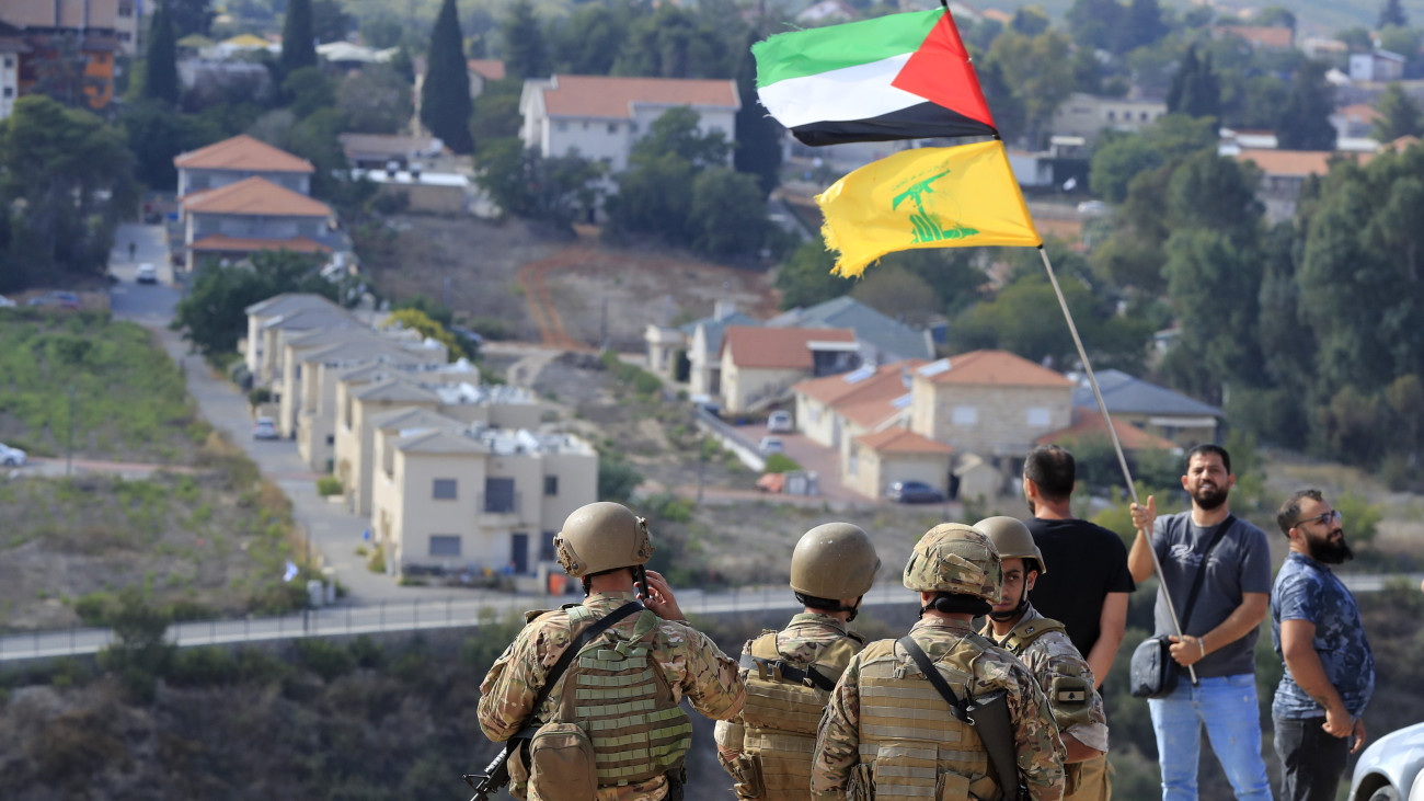 A Palesztin Állam és a Hezbollah radikális libanoni síita szervezet zászlóit lengeti egy férfi libanoni katonák előtt az izraeli-libanoni határon fekvő Kfar Kilában 2023. október 9-én. A Gázai övezetet irányító Hamász palesztin iszlamista szervezet október 7-én többfrontos támadást indított Izrael ellen, több mint 800 izraeli életét vesztette, a Hamász elleni izraeli válaszcsapások halálos áldozatainak száma a Gázai övezetben 500, a sebesülteké meghaladja a háromezret. Az izraeli hadsereg ellencsapásokat hajtott végre a libanoni határnál is.