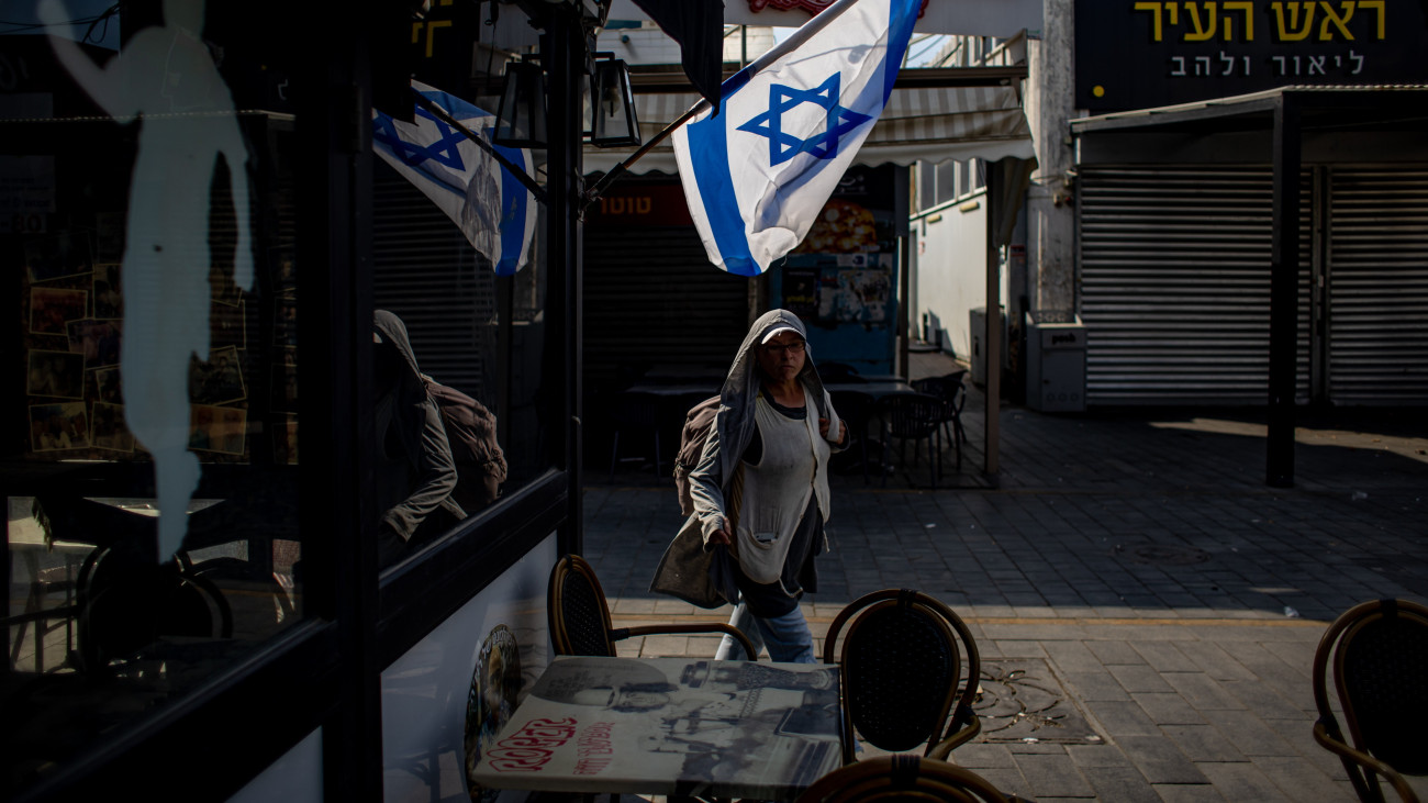 Kávézóra kitűzött izraeli zászló alatt megy el egy nő a dél-izraeli Askelónban 2023. október 16-án. Az izraeli hadsereg szárazföldi hadműveletre készül a Hamász ellen, mert a Gázai övezetet irányító palesztin iszlamista szervezet október 7-én többfrontos támadást intézett Izrael ellen, ahol több mint 1300 ember életét vesztette.