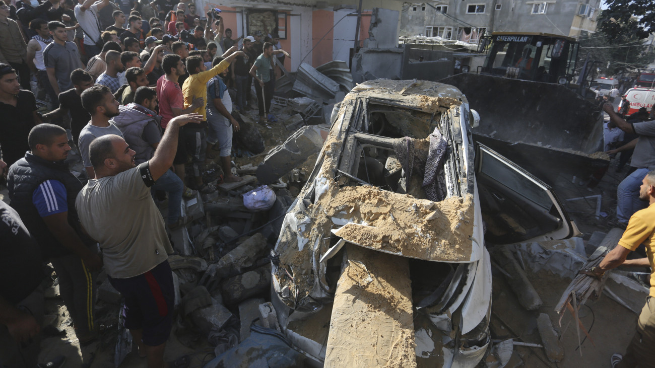 Izraeli légitámadásban szétroncsolódott autót eltávolító buldózert néznek palesztinok a Gázai övezet déli részén fekvő Rafahban 2023. október 30-án. A Gázai övezetet irányító Hamász palesztin iszlamista szervezet október 7-én többfrontos támadást indított Izrael ellen, az izraeli légierő azóta támadja a Hamász katonai létesítményeit a palesztinok lakta övezetben. Izraelben több mint 1400 ember életét vesztette, az izraeli válaszcsapások több mint 8000 palesztin halálát okozták a Gázai övezetben.