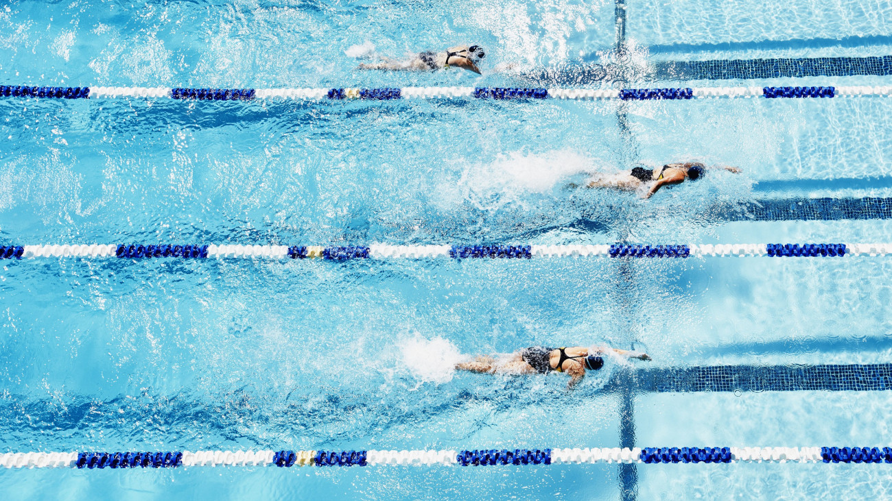 Young female competitive swimmers racing in outdoor pool overhead view