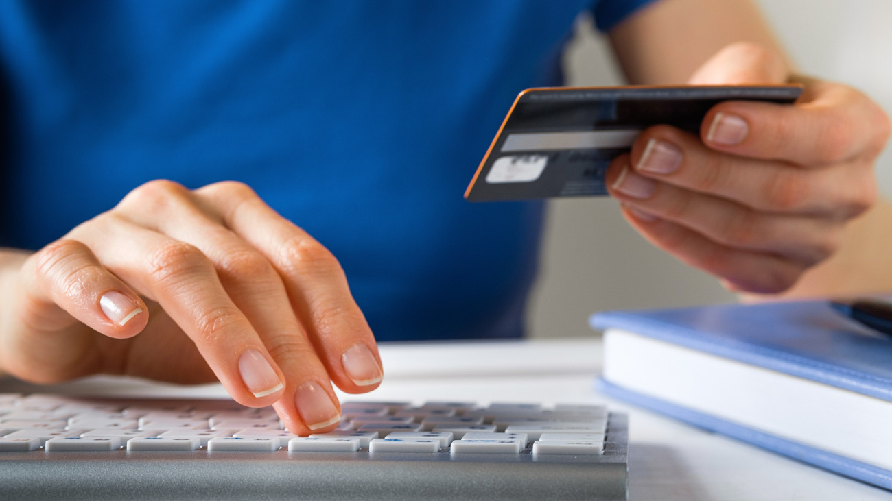 A Woman Is Holding A Credit Card, Typing on A Laptop Keyboard. Theres a Notepad and a Pen next to it. The Concept of Buying Online, Ordering Products at Home, and paying via the Internet.