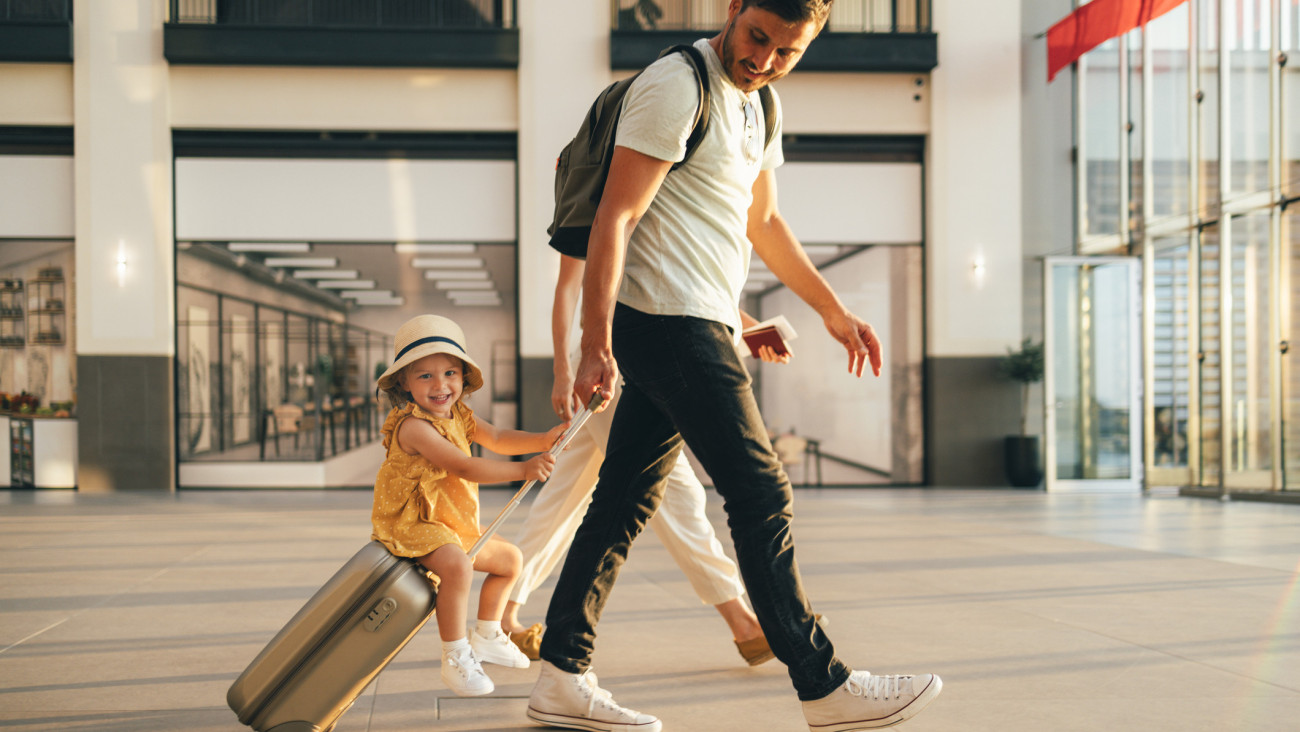 Cheerful husband and his anonymous wife walking with their little girl sitting on luggage at the airport.