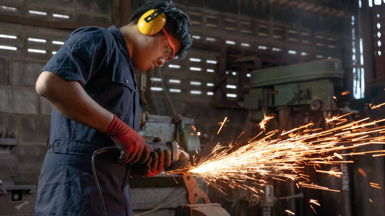 Engineer operating angle grinder hand tools in manufacturing factory - Mechanical engineering student using power tool with hot metal sparks wearing safety equipment - workshop and occupation concept. Getty Images