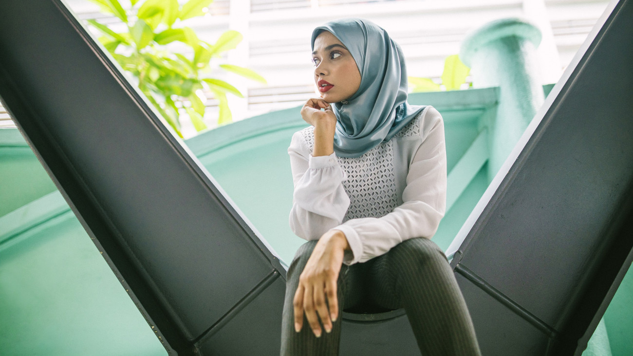Close up of young, pretty Muslim woman, well-dressed, with hijab, sitting and looking away