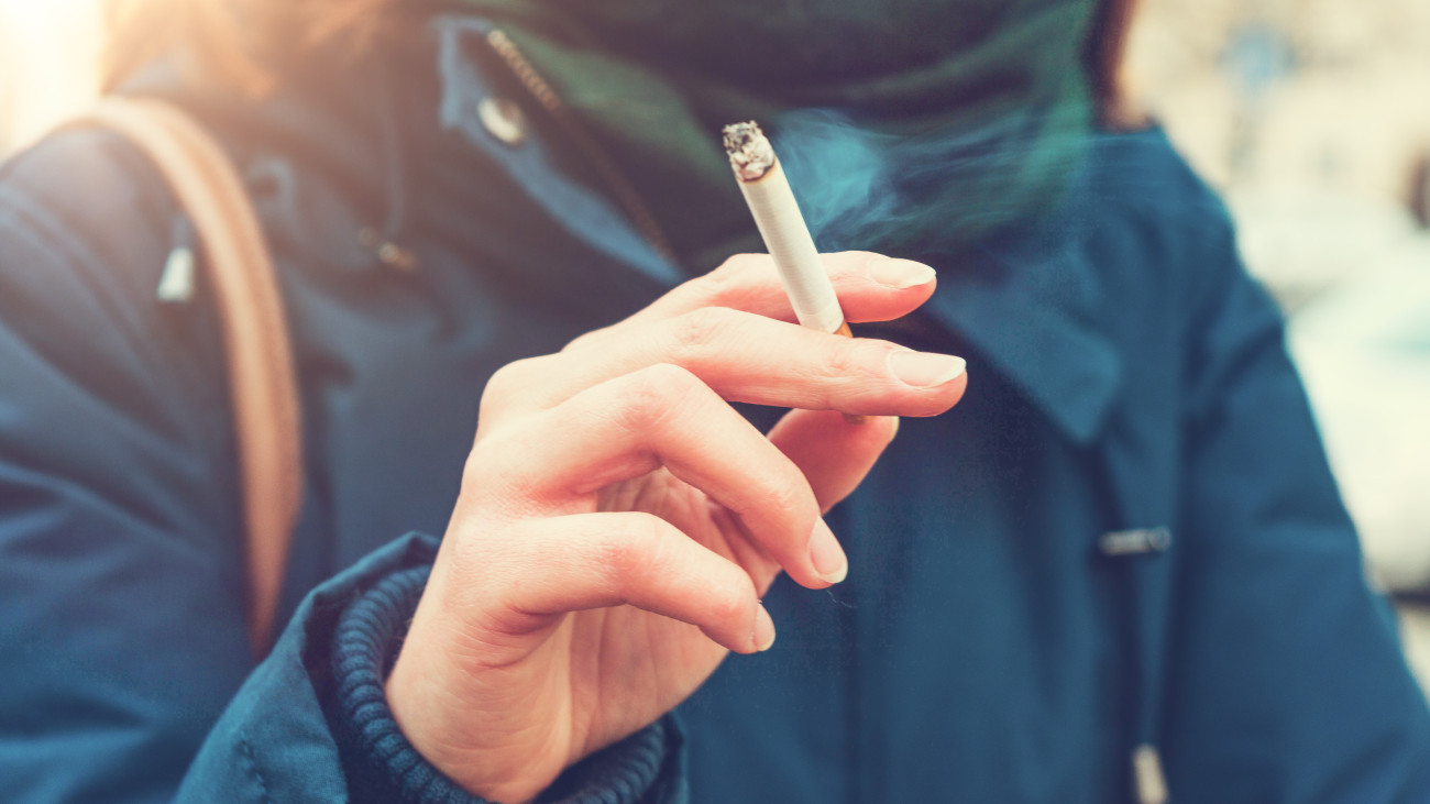 Young woman enjoying a cigarette outdoors holding it between her fingers, low angle view against the chest of a warm autumn jacket in a smoking and tobacco concept