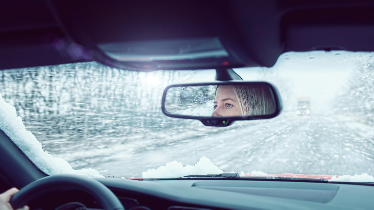 Woman driving car through winter snow on road in the UK.