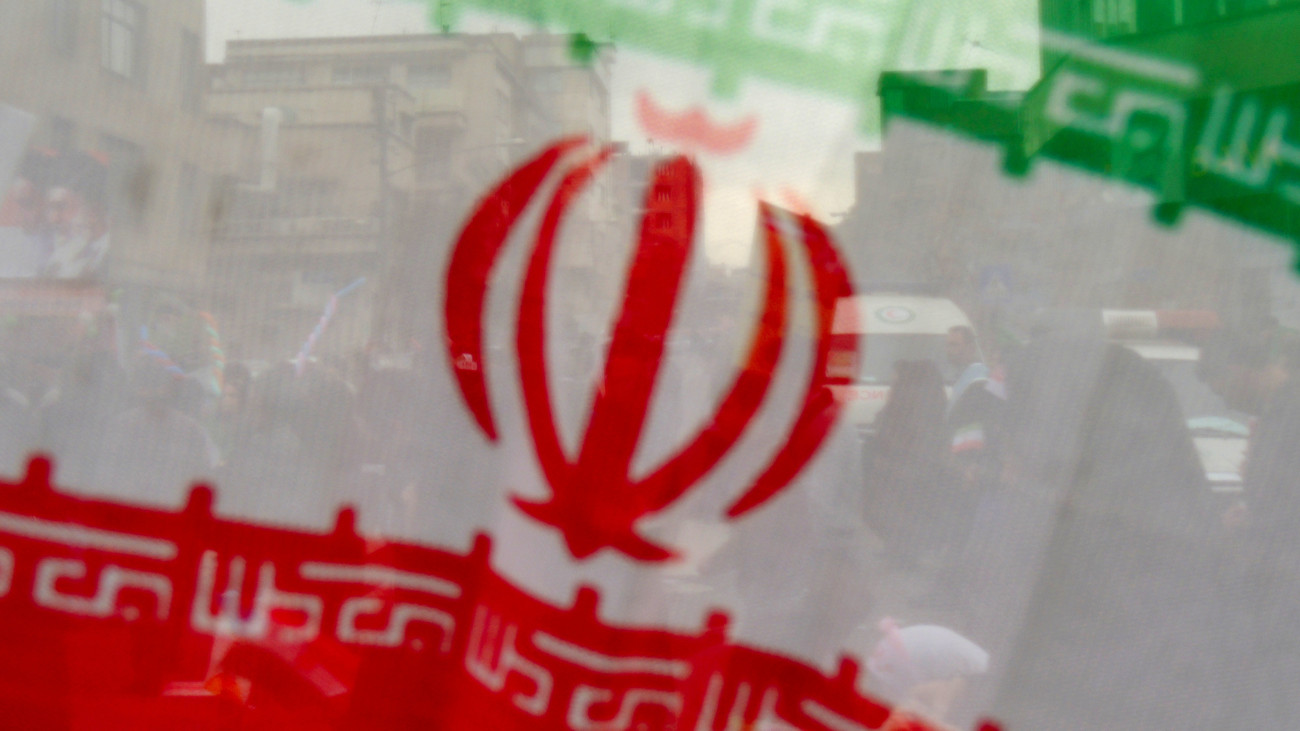 Wavy and slanted Iranian flag in the front plane, with masses of Iranian people behind who celebrate an anniversary of the 1979 Islamic Revolution and Iranian independence day, in a march along Azadi avenue toward Azadi square every 22nd of Bahman or 10-11th of February.