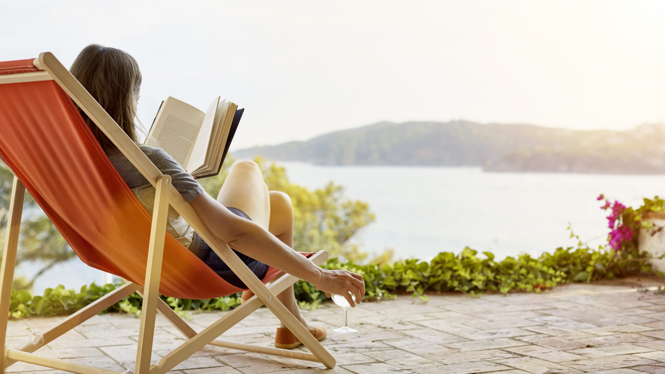 Woman reading book while relaxing on deck chair at back yard
