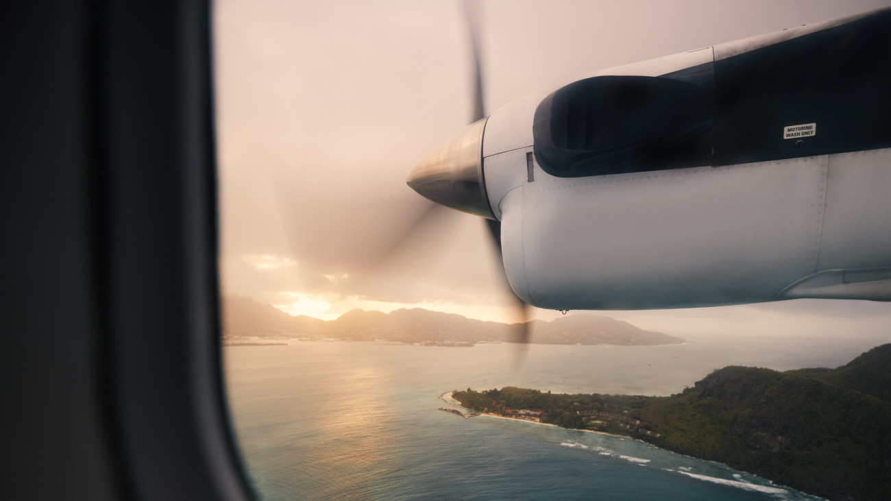 View from propeller airplane window during flight above Seychelles islands at beautiful sunset.