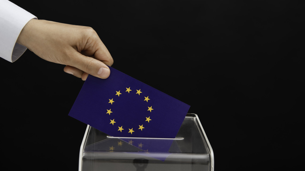 Human hand is inserting European Union flag into ballot box in front of black background. Representing elections in  European Union.