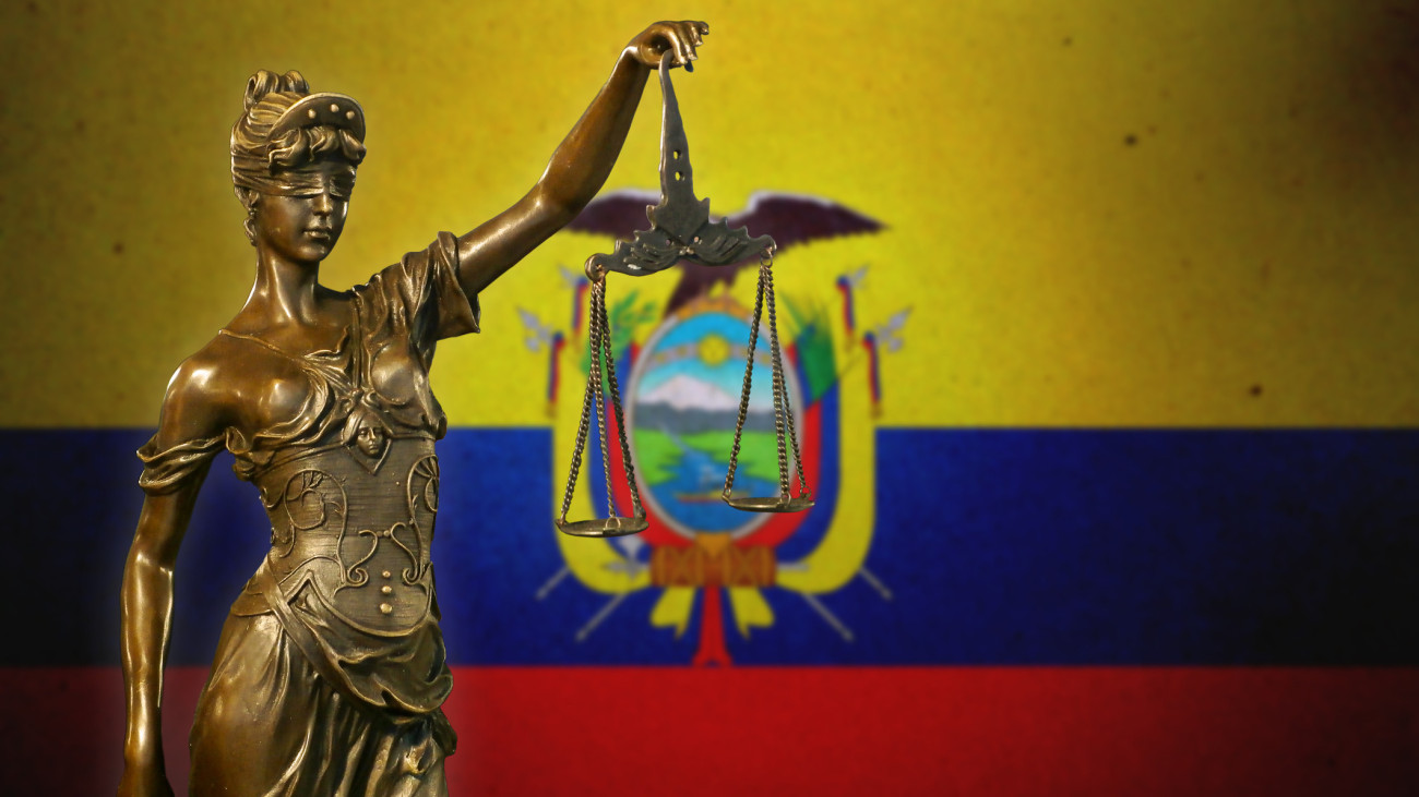 Close-up of a small bronze statuette of Lady Justice before a flag of Ecuador.